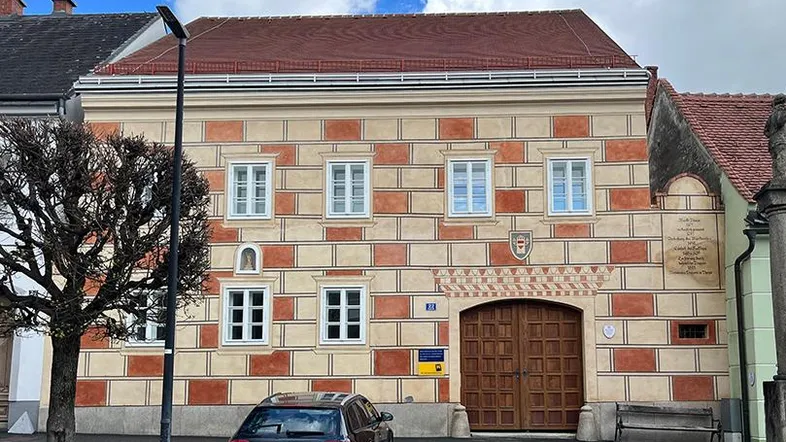 Historisches Gebäude mit markanter Fassadenmalerei und großem Holztor an einer Straße.