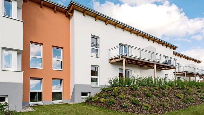 Moderne Wohnanlage mit weißer und oranger Fassade, Balkonen und gepflegter Grünfläche.