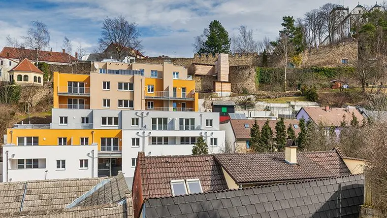 Panoramablick auf moderne Wohngebäude mit farbigen Fassaden und die umliegende hügelige Landschaft.