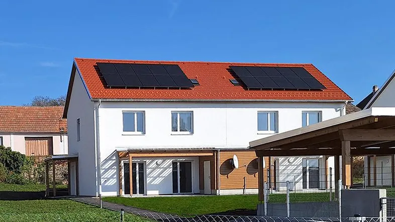 Modernes Einfamilienhaus mit weißer Fassade, rotem Dach und Photovoltaikanlage im Grünen.