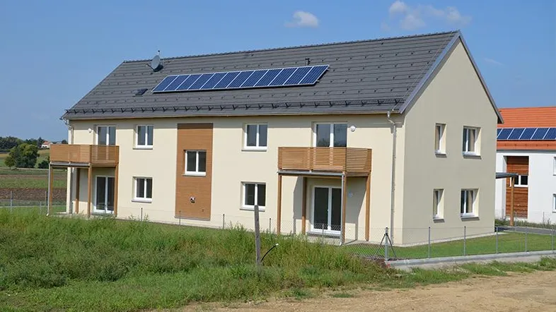 Modernes Reihenhaus mit beiger Fassade, Solarpaneelen auf dem Dach und Holzbalkonen.