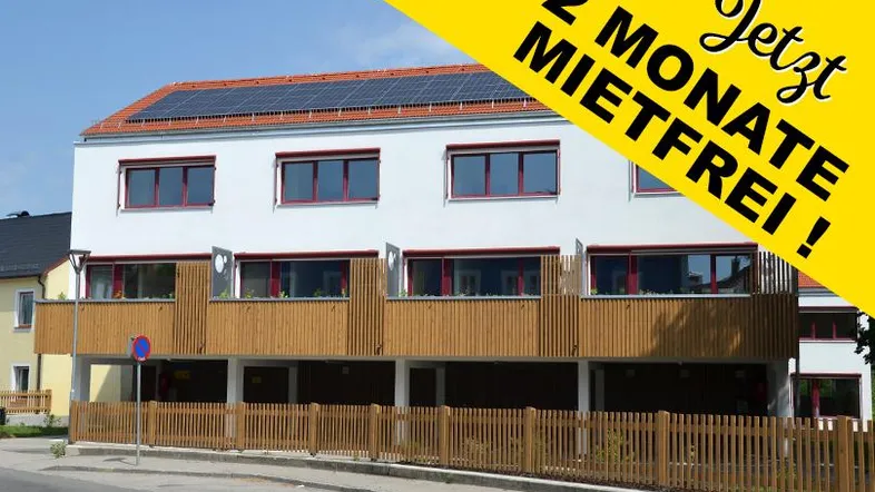 Modernes Mehrfamilienhaus mit weißer Fassade, Holzverkleidung und Solaranlage auf dem Dach.