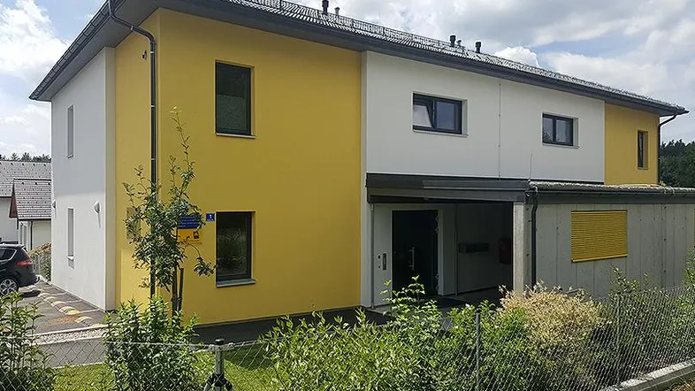 Modernes Mehrfamilienhaus mit gelb-weißer Fassade und gepflegter Außenanlage unter blauem Himmel.