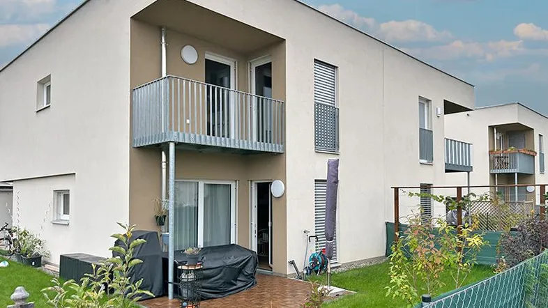 Moderne Reihenhausfassade mit Balkonen und einer möblierten Terrasse im Erdgeschoss.