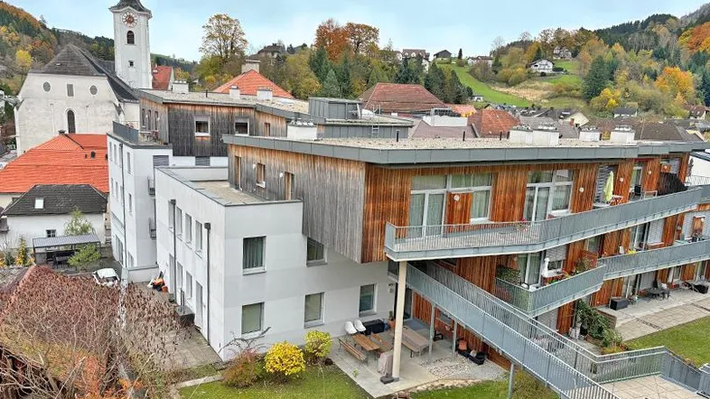 Moderne Wohnanlage mit Holzfassade und Blick auf die umliegende Landschaft und Kirche.