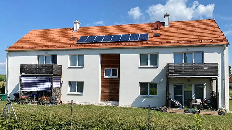 Vorderansicht eines Wohngebäudes mit weißer Fassade, rotem Ziegeldach und Solarpaneelen.