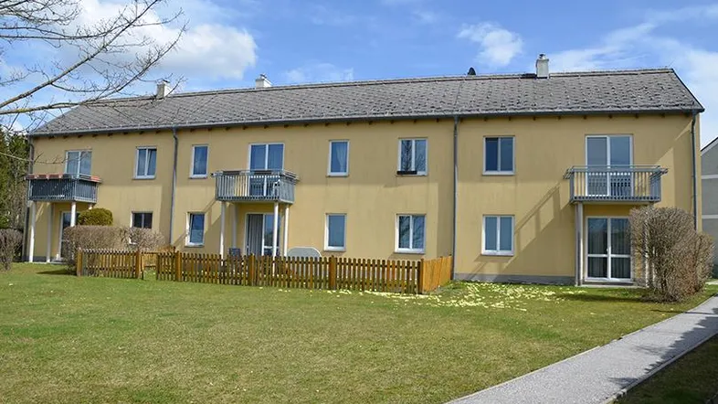 Mehrfamilienhaus mit gelber Fassade, Balkonen und einem gepflegten Rasenbereich davor.