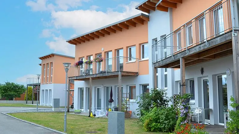 Moderne Reihenhäuser mit orangefarbenen Fassaden, Balkonen und kleinen Gärten unter blauem Himmel.