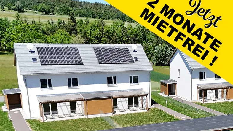 Moderne Reihenhäuser mit Solarpaneelen auf dem Dach in grüner Umgebung, mit Werbebanner.