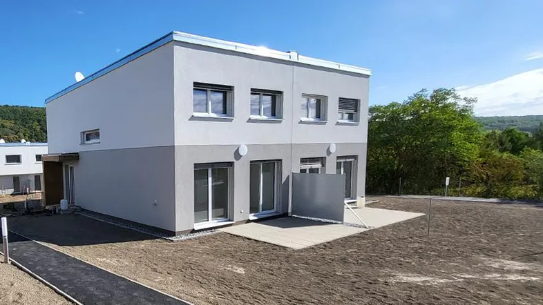 Modernes Reihenhaus mit heller Fassade, kleiner Terrasse und vorbereitetem Gartenbereich.