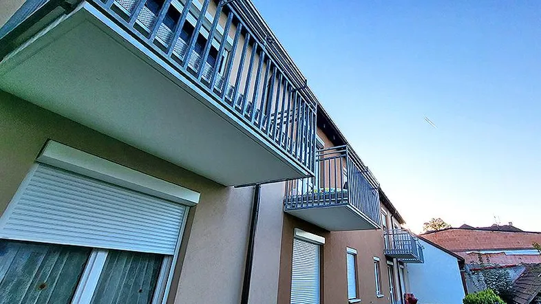 Die moderne Fassade des Gebäudes mit mehreren Balkonen und Rollläden unter blauem Himmel.