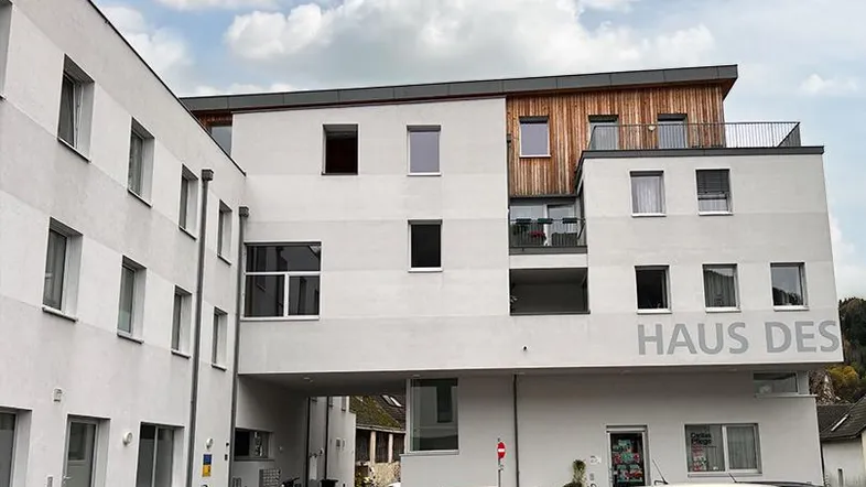 Moderne Wohnanlage mit weißer Fassade, Holzverkleidung und Balkonen unter bewölktem Himmel.