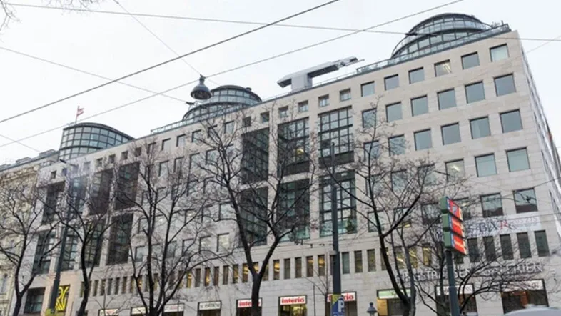 Großes Geschäftsgebäude mit moderner Architektur, vielen Fenstern und Geschäften im Erdgeschoss unter bewölktem Himmel.