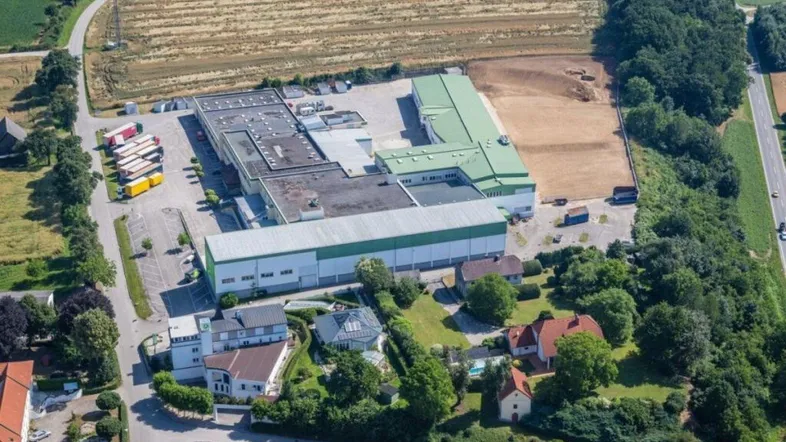Luftaufnahme eines großen Industrie- und Gewerbekomplexes umgeben von Feldern und Bäumen.