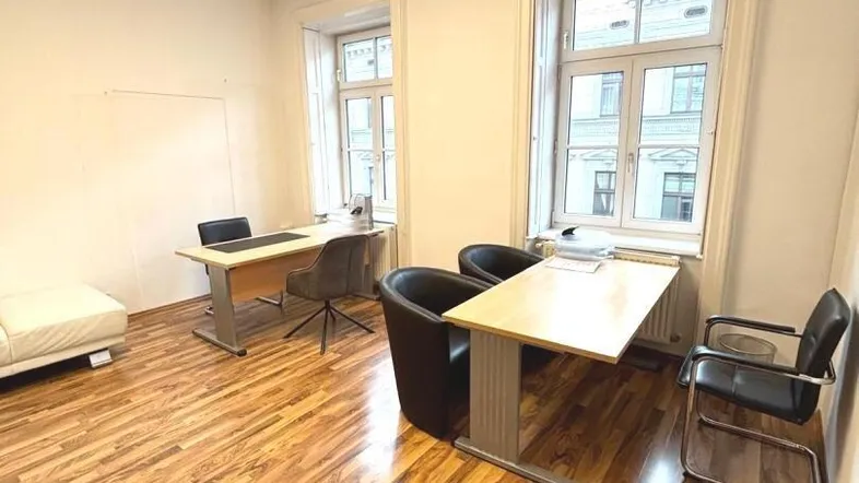 Helles Büro mit Holzboden, zwei Arbeitsplätzen und einer weißen Couch.