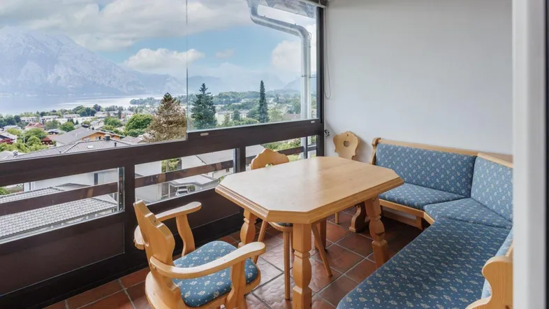 Gemütlicher Balkon mit Holztisch, Sitzbank und einem atemberaubenden Blick auf den See und die Berge.