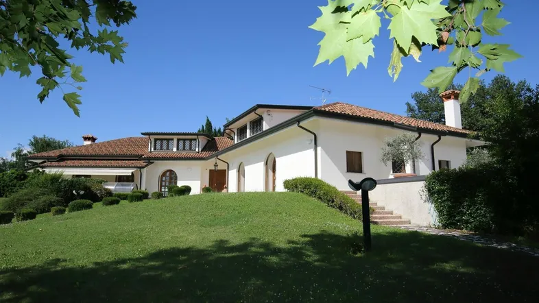 Weiße Villa mit Terrakottadach und gepflegtem Rasen unter blauem Himmel.