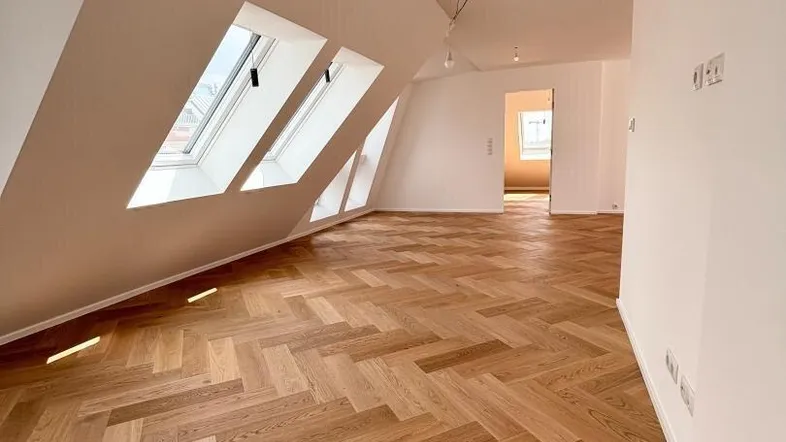 Helles Zimmer im Dachgeschoss mit Fischgrätparkett, Dachfenstern und schrägen Wänden.