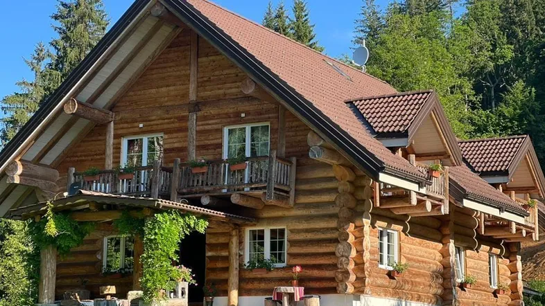 Charmantes Blockhaus mit Holzbalkonen und Satteldach, umgeben von grünen Bäumen und Wiesen.