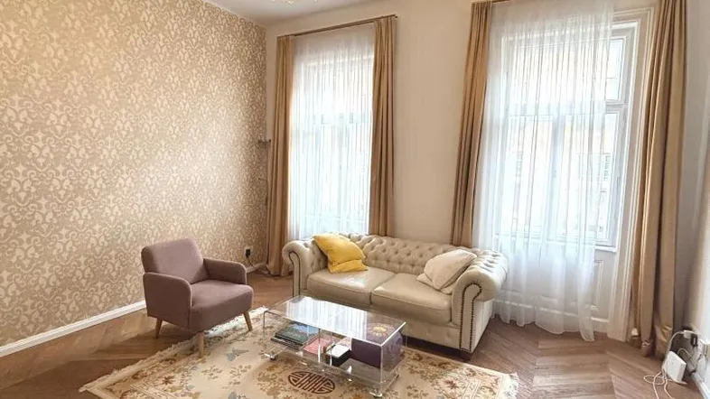 Helles Wohnzimmer mit elegantem Kronleuchter, gemusterter Tapete und Fischgrätparkett.