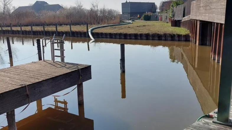 Hölzerne Stege und Terrassen am Wasser mit Blick auf die umliegende Natur und moderne Gebäude.