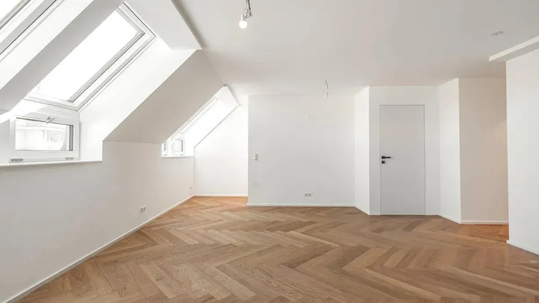 Heller Raum im Dachgeschoss mit Fischgrätparkett, weißen Wänden und schrägen Dachfenstern.