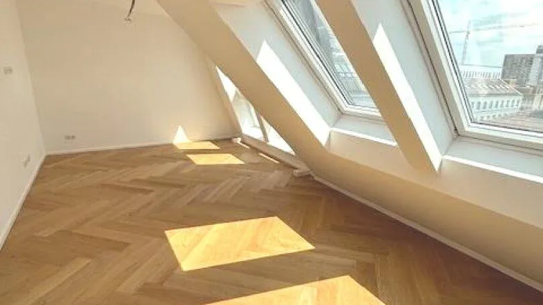 Helles Zimmer im Dachgeschoss mit Fischgrätparkett, hohen Decken und großen Dachfenstern.