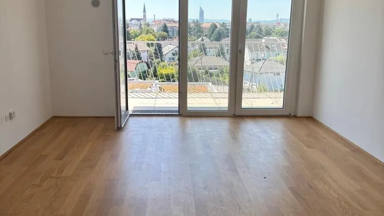 Helles Zimmer mit Holzboden und Zugang zu einem Balkon mit weitem Stadtblick.