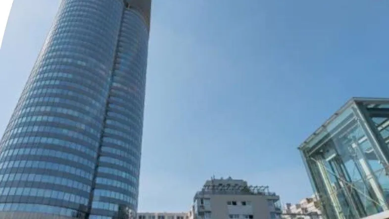 Ein modernes Hochhaus mit Glasfassade und umliegenden Gebäuden unter blauem Himmel.