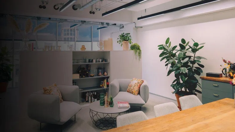 Moderner Bürobereich mit bequemen Sitzgelegenheiten, Pflanzen und industrieller Deckenbeleuchtung für eine angenehme Arbeitsatmosphäre.