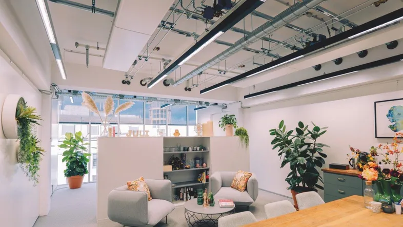 Moderner Bürobereich mit Lounge-Möbeln, vielen Pflanzen und freiliegenden Deckeninstallationen.