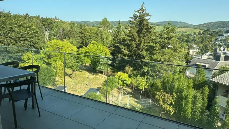 Geräumiger Balkon mit Glasgeländer, Essbereich im Freien und weitem Blick ins Grüne.