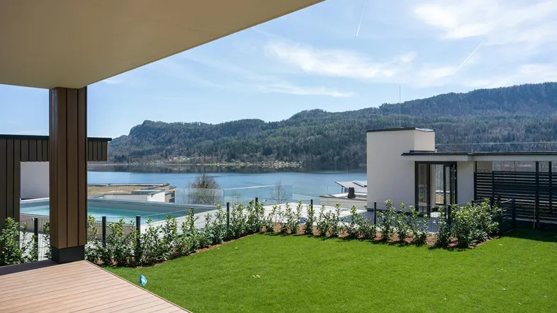 Moderne Holzterrasse mit Rasenfläche und weitem Blick auf den See und die umliegenden Berge.