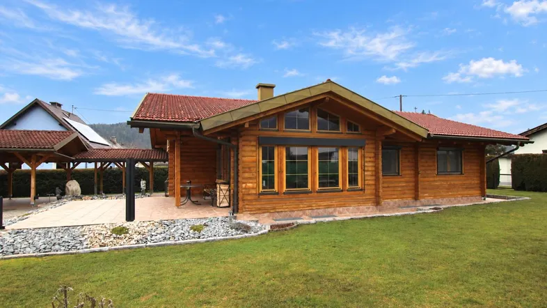 Blockhaus-Stil Einfamilienhaus mit Holzfassade, rotem Ziegeldach und gepflegtem Rasen.