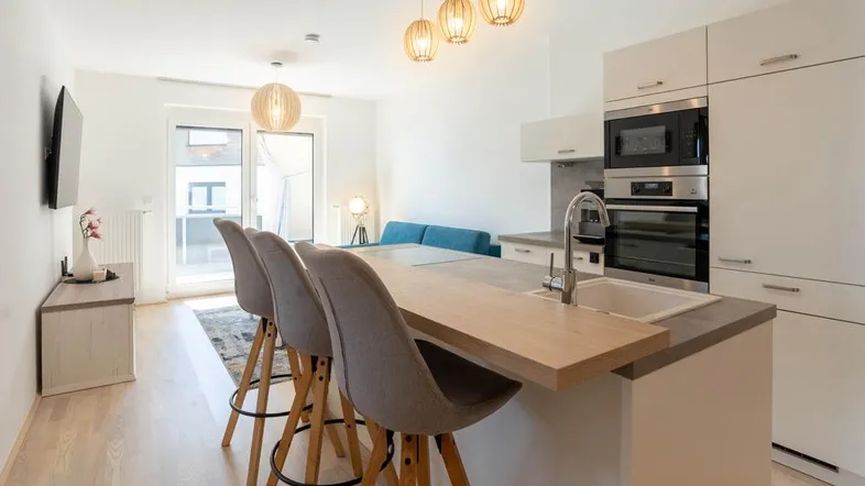Heller offener Wohn- und Essbereich mit moderner Küche, Kücheninsel und Zugang zum Balkon.