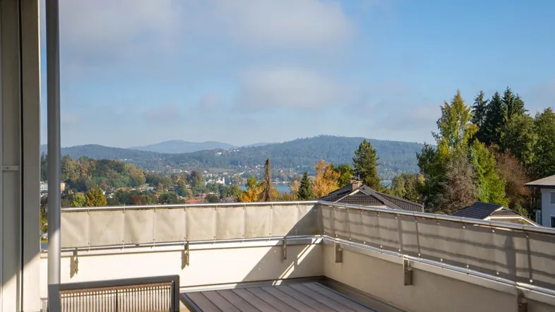 Geräumiger Balkon mit Holzboden, Esstisch und weitem Blick über die Landschaft und Berge.