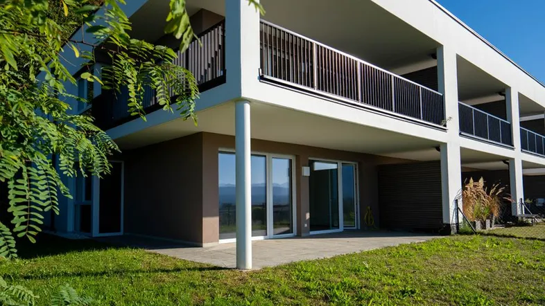Moderne Wohnanlage mit Terrassen, Balkonen und Bergblick, umgeben von Grünflächen.