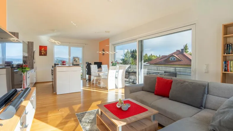 Heller, offener Wohn-Essbereich mit integrierter Küche, Holzboden und Zugang zum Balkon mit Weitblick.