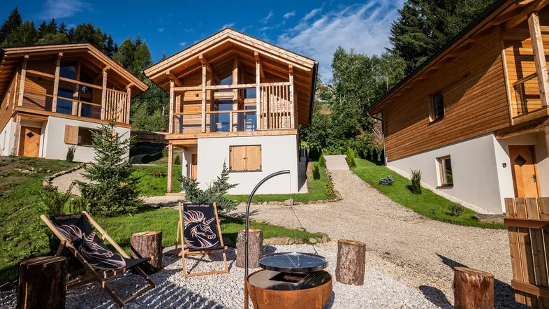 Mehrere moderne Holzchalets auf einem Hügel mit Außenbereich und Grillplatz unter blauem Himmel.