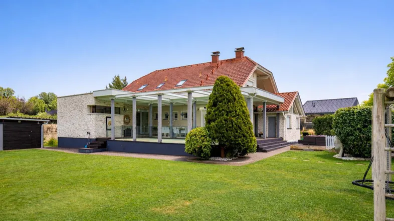 Weitläufiger Garten mit großer Rasenfläche und überdachtem Terrassenbereich am Haus.