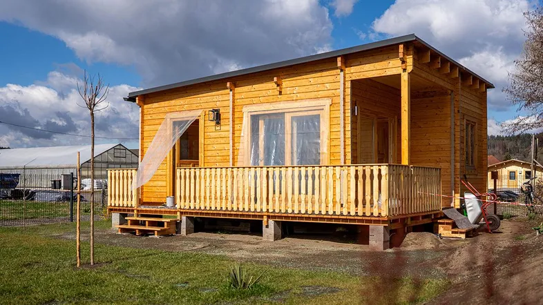 Kleines Holzhaus mit überdachter Terrasse und Blick auf die Umgebung unter blauem Himmel.