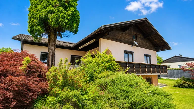 Traditionelles Haus mit Holzbalkon und üppiger Vegetation unter strahlend blauem Himmel.