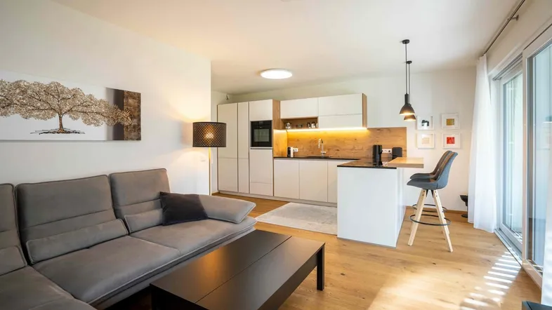 Heller offener Wohnbereich mit moderner Küche, Parkettboden und Zugang zum Balkon.