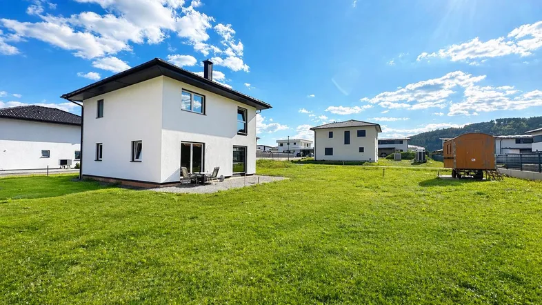 Neubau-Einfamilienhaus mit großem Garten und sonniger Terrasse unter blauem Himmel.