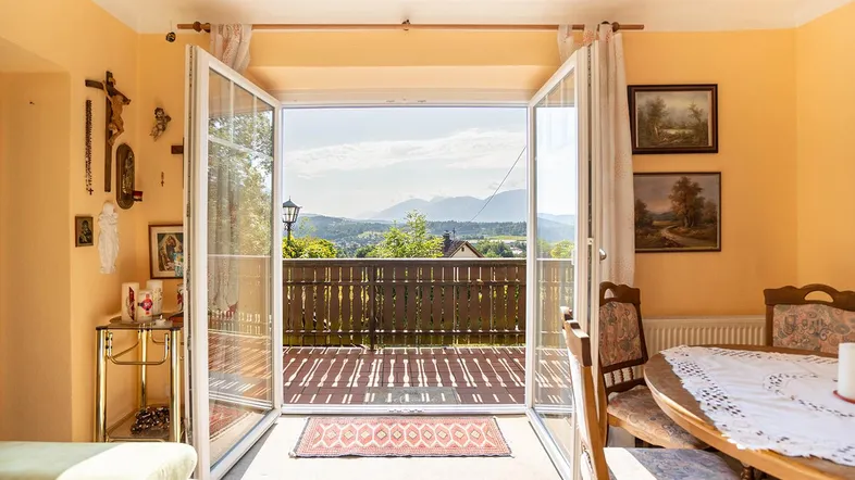 Helles Wohn- und Esszimmer mit Zugang zum Balkon und weitem Blick auf die umliegende Berglandschaft.