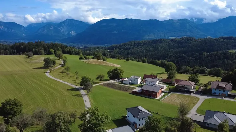 Weitläufige Landschaft mit grünen Hügeln, vereinzelten Häusern und majestätischen Bergen im Hintergrund.