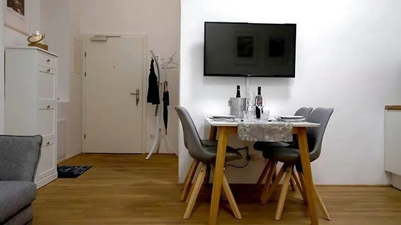Heller Wohn- und Essbereich mit Esstisch, Wandfernseher und Zugang zum Eingangsbereich.