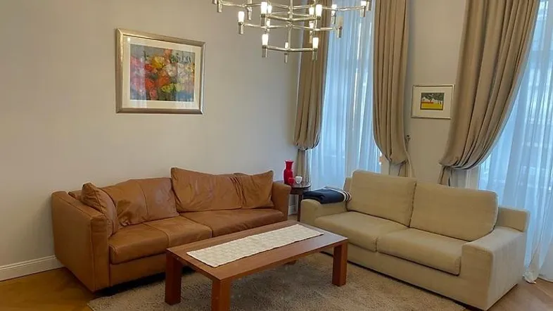 Helles Wohnzimmer mit bequemen Sofas, Parkettboden und einem modernen Kronleuchter.
