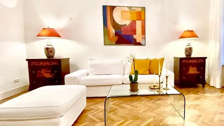 Helles Wohnzimmer mit Fischgrätparkett, weißem Sofa und farbenfrohem Kunstwerk an der Wand.