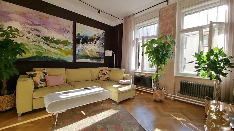 Helles Wohnzimmer mit bequemer Couch, Kunstwerken an der Wand und großen Fenstern.